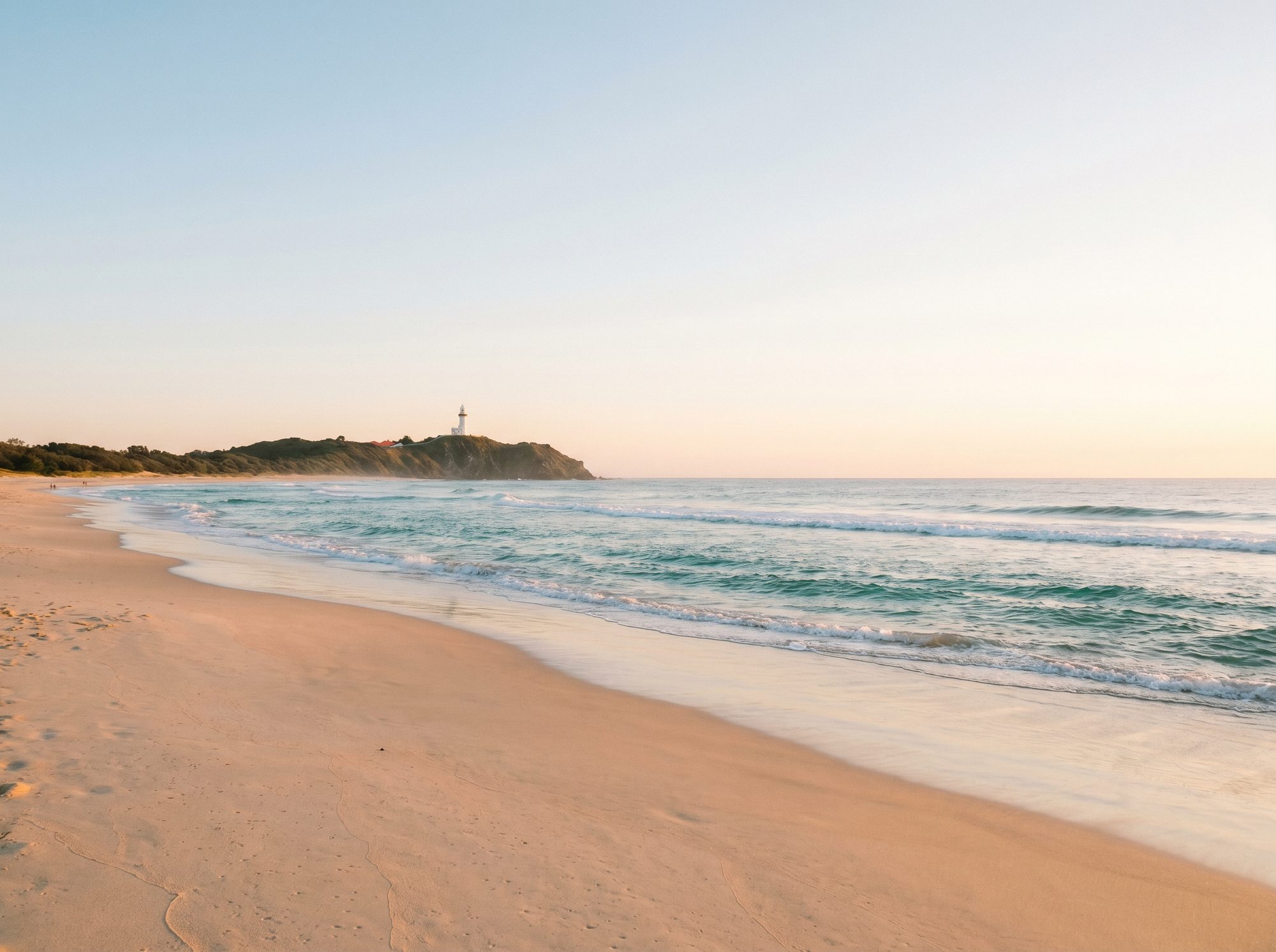 Byron Bay beach at golden hour with lighthouse on the headland in the distance